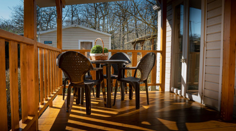 Sunny porch at Mobile home Urederra, Camping Etxarri, Spain, featuring plastic chairs and a round table.