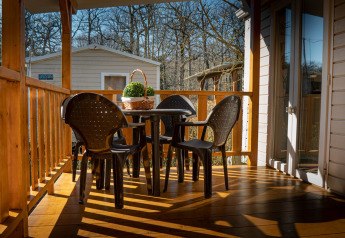 Zonnige veranda bij Mobile home Urederra op Camping Etxarri in Spanje met plastic stoelen en ronde tafel.