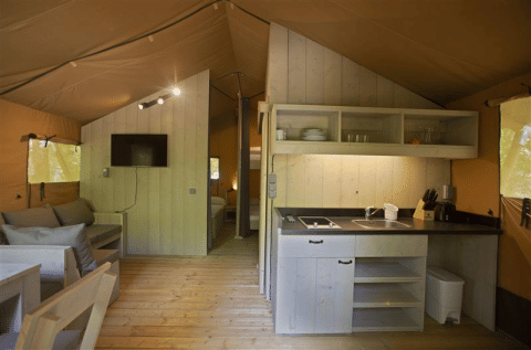 Interior de la tienda safari Glamping Haritza en Camping Etxarri, España, con cocina y zona de estar.
