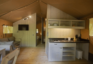 Interior de la tienda safari Glamping Haritza en Camping Etxarri, España, con cocina y zona de estar.