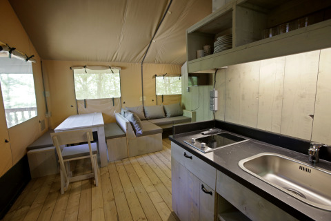 Interior de una tienda safari Glamping Haritza en Camping Etxarri, España, con cocina y zona de descanso visibles.
