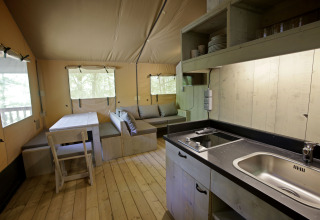 Interior de una tienda safari Glamping Haritza en Camping Etxarri, España, con cocina y zona de descanso visibles.