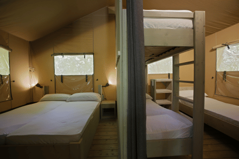 Interno di una tenda safari al Glamping Haritza, Camping Etxarri in Spagna, con letto matrimoniale e letti a castello.