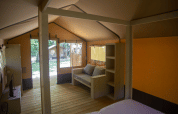 Interior view of a safari tent, Glamping Jare, at Camping Etxarri in Spain, showing sofa and wood shelves.