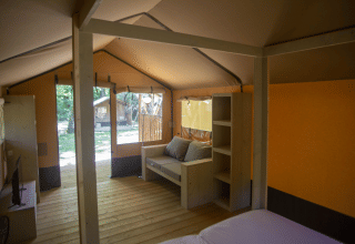 Interior view of a safari tent, Glamping Jare, at Camping Etxarri in Spain, showing sofa and wood shelves.