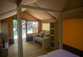 Interior view of a safari tent, Glamping Jare, at Camping Etxarri in Spain, showing sofa and wood shelves.