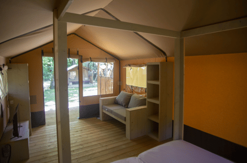 Interior view of a safari tent, Glamping Jare, at Camping Etxarri in Spain, showing sofa and wood shelves.