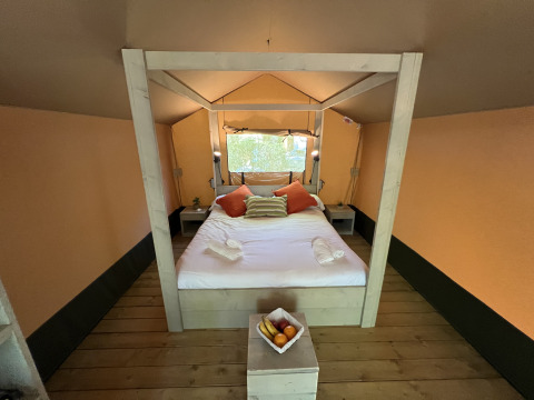 Vista interior de una cama acogedora en la tienda safari Glamping Jare en Camping Etxarri, España, con decoración de madera.