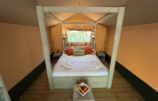 Vista interior de una cama acogedora en la tienda safari Glamping Jare en Camping Etxarri, España, con decoración de madera.