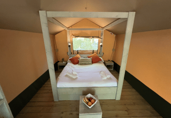 Vista interna di un letto accogliente nella tenda safari Glamping Jare al Camping Etxarri, Spagna, con arredi in legno.