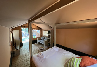 Interno di una tenda safari di lusso a Glamping Jare, Camping Etxarri, Spagna, con letto e salotto accoglienti.