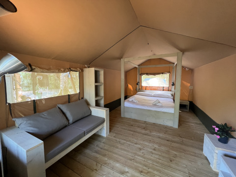 Vista interna di una tenda safari con letto matrimoniale, divano e pavimento in legno a Glamping Jare, Camping Etxarri.