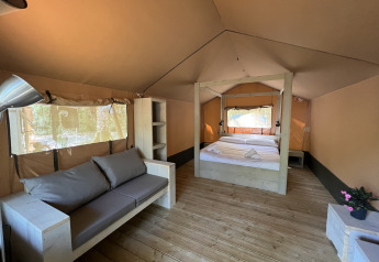Interior view of a safari tent with double bed, sofa, and wooden floor at Glamping Jare, Camping Etxarri.