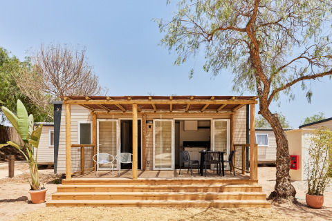 Foto del Bungalow Premium Agave con terraza de madera, sillas exteriores y árboles alrededor en un día soleado.