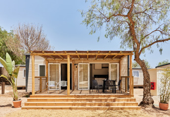 Foto del Bungalow Premium Agave con terraza de madera, sillas exteriores y árboles alrededor en un día soleado.