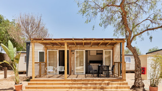 Foto del Bungalow Premium Agave con terraza de madera, sillas exteriores y árboles alrededor en un día soleado.