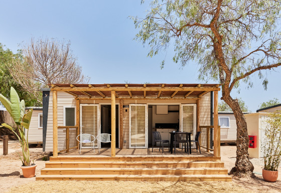 Foto del Bungalow Premium Agave con terraza de madera, sillas exteriores y árboles alrededor en un día soleado.