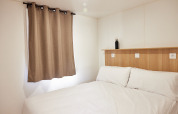 Dormitorio minimalista en cabaña, con cama doble, paredes blancas, cortinas beige y cabecero de madera.