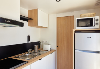 Moderne chaletkeuken met gootsteen, kookplaat, microgolf, koelkast, broodrooster en lichte houtlook.