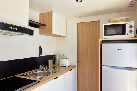 Cocina moderna de cabaña con fregadero, placa, microondas, nevera, tostadora y muebles de madera clara.