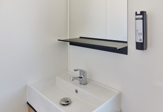 Lavabo moderno con grifo, espejo, estante y dispensador de jabón en un baño de una cabaña.