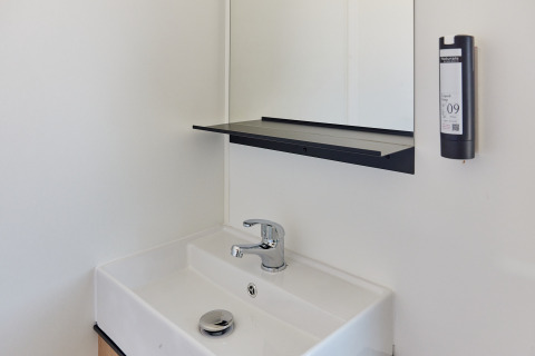 Moderne håndvask med spejl, hylde og sæbedispenser i et minimalistisk badeværelse i en hytte.