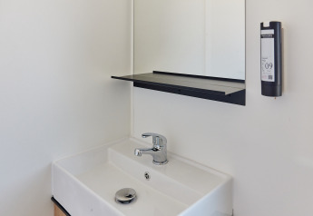 Moderne wastafel met kraan, spiegel, plankje en zeepdispenser in een badkamer van een hut.