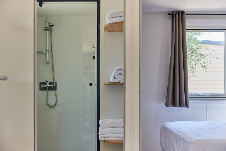 Baño moderno de cabina con puerta de ducha de cristal, toallas limpias y vista al dormitorio.