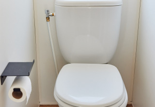 Et rent moderne toilet med toiletpapirholder og vindue i en hytte med trægulv og lyse vægge.