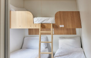 Efficient cabin room with three beds: two single beds below and one lofted bunk bed accessed by ladder.