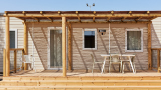 Terraza de madera con sillas y mesa frente al Bungalow Premium Agave, parcialmente sombreada, soleado.