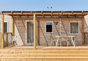 Terraza de madera con sillas y mesa frente al Bungalow Premium Agave, parcialmente sombreada, soleado.