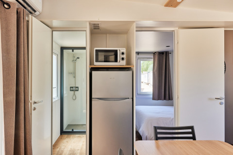 Interior del Bungalow Premium Agave en TAIGA Almería Playa con frigorífico, microondas, ducha y dormitorio.