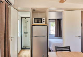 Interior del Bungalow Premium Agave en TAIGA Almería Playa con frigorífico, microondas, ducha y dormitorio.