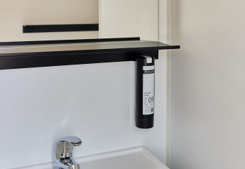 Moderno lavabo de baño con espejo y dispensador de jabón en Bungalow Premium Agave, TAIGA Almeria Playa, España.