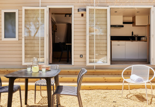 Buiten eetruimte aan Bungalow Confort Agave met tafel, stoelen, terras en zicht op de keuken.