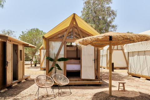 Tienda safari Glamping Tent Palmeral con cama acogedora, sillas modernas y sombrilla de paja al aire libre.