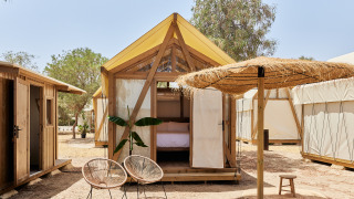 Tenda safari Glamping Tent Palmeral con letto accogliente, sedie moderne e ombrellone di paglia all'aperto.