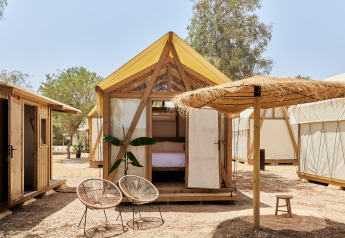 Tenda safari Glamping Tent Palmeral con letto accogliente, sedie moderne e ombrellone di paglia all'aperto.