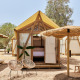 Tienda safari Glamping Tent Palmeral con cama acogedora, sillas modernas y sombrilla de paja al aire libre.