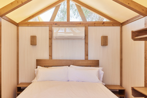 Interior de una tienda glamping safari con cama cómoda y detalles de madera en TAIGA Almeria Playa, España.