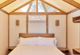 Interior de una tienda glamping safari con cama cómoda y detalles de madera en TAIGA Almeria Playa, España.