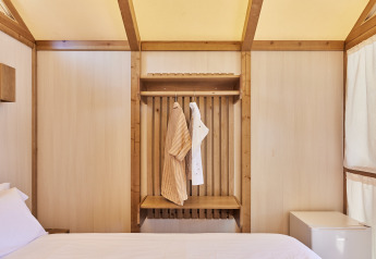 Interno della tenda glamping Palmeral al TAIGA Almeria Playa con letto, vestiti appesi e mini frigo.