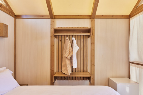 Interior de la Tienda Glamping Palmeral en TAIGA Almería Playa con cama, ropa colgada y mini nevera.