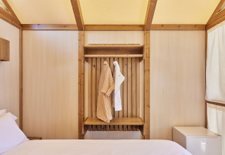 Interior de la Tienda Glamping Palmeral en TAIGA Almería Playa con cama, ropa colgada y mini nevera.