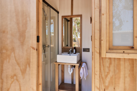 Badkamer in een safaritent met vierkante lavabo, spiegel, douche en houten decoratie.