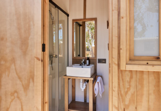 Badkamer in een safaritent met vierkante lavabo, spiegel, douche en houten decoratie.