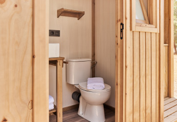Bagno moderno in una tenda safari con WC, asciugamani e finiture in legno, visto dall’esterno.