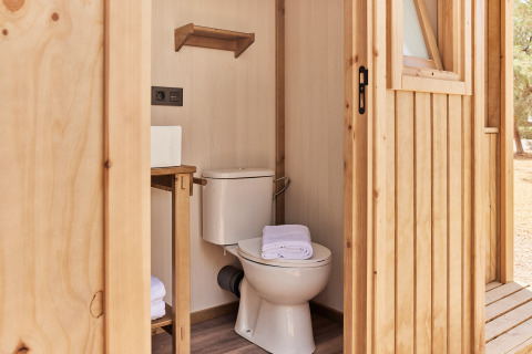 Et moderne badeværelse i et safaritelt med toilet, håndklæder og træindretning, set udefra.