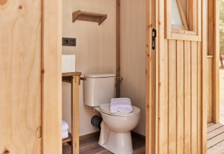 Et moderne badeværelse i et safaritelt med toilet, håndklæder og træindretning, set udefra.